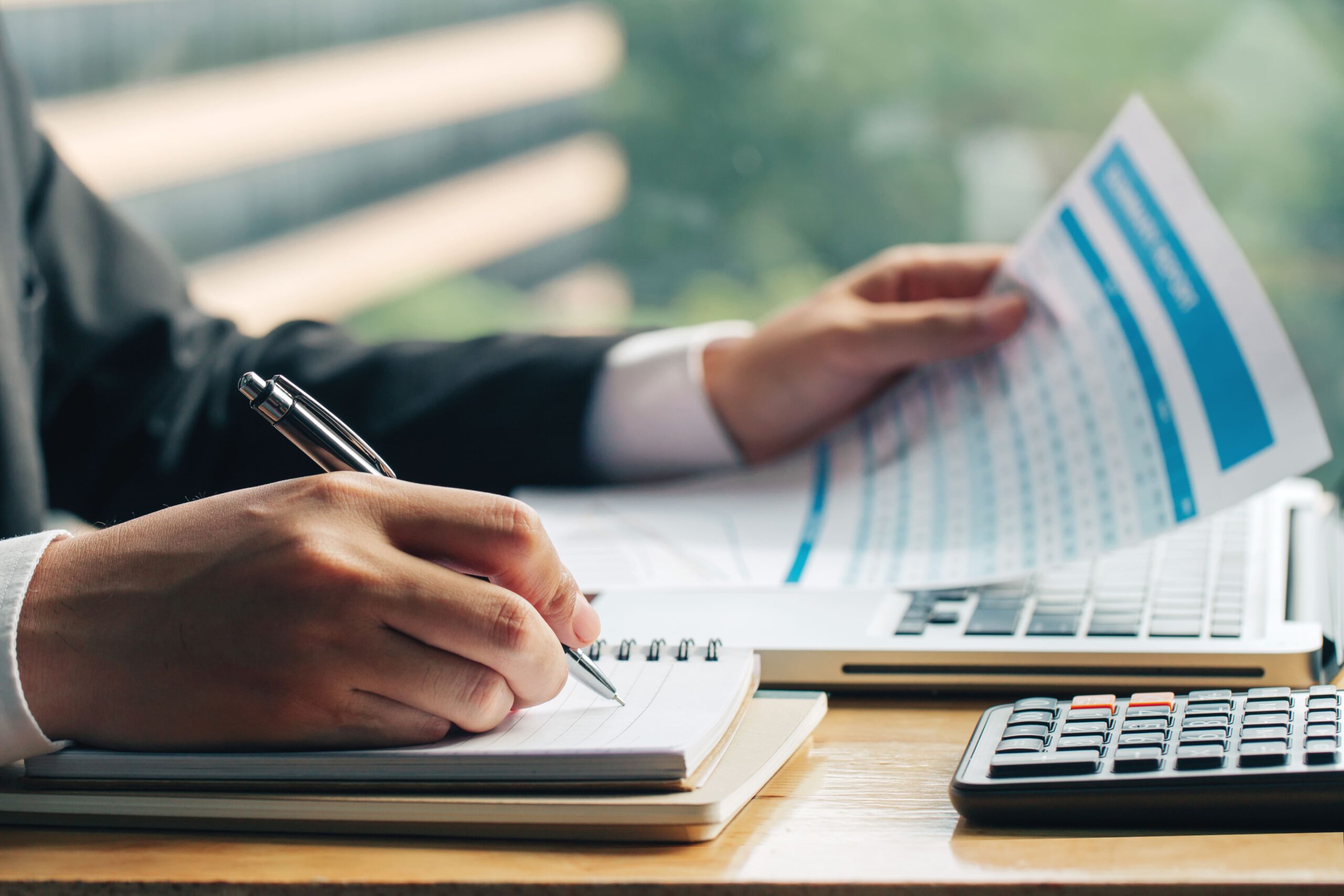 close-up-shot-of-business-man-hands-with-pen-writing-notes-on-paper-and-other-hand-holding-the-marketing-chart (1)